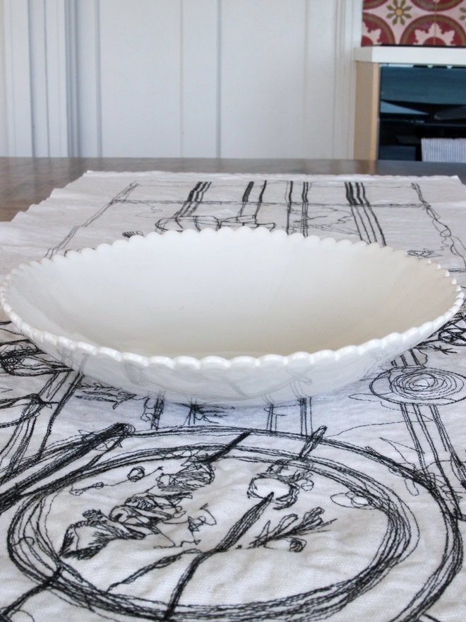 white scalloped edge serving bowl for fruit or salad on a table setting with black and white tablecloth