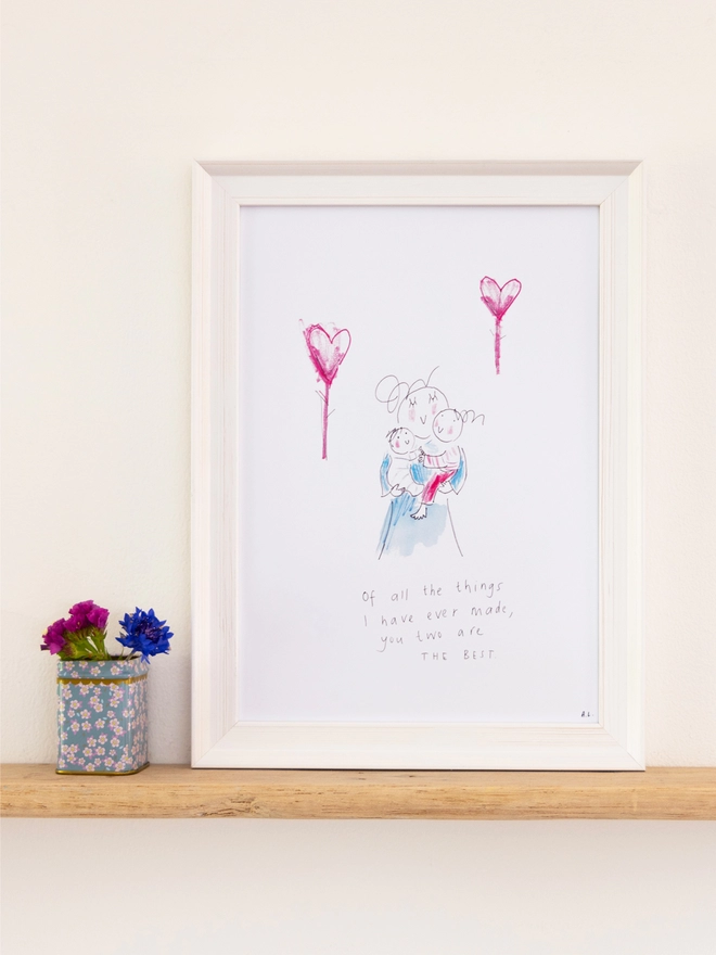 a sketchy muma print in a white frame next to a small tin of flowers