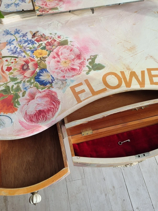 An antique kidney-shaped dressing table with chair and a trio of mirrors. Upcycled in cream and pale pink with decoupage florals in oranges and pinks. Text across the table read ‘flowers make me happy’ in the orange of the undercoat.