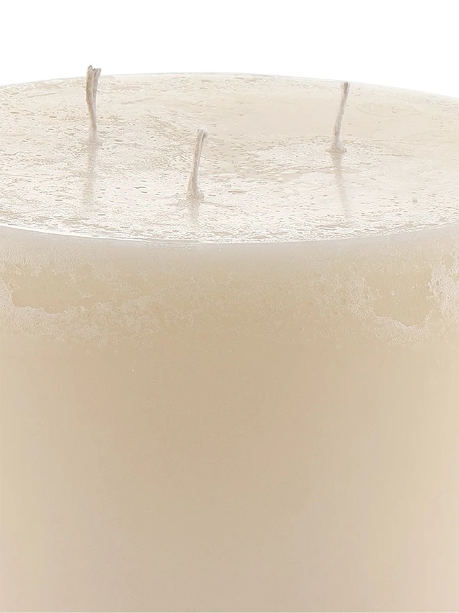 Jasmine, Green Tea & Mulberry Candle (Set Of 1 Or 3 Wicks). a close-up shot of the oudh, yuzu and patchouli candle shows the top of the cream wax pillar, with three wicks and a textured, slightly uneven surface. drip marks run down the side of the candle, adding to its handmade, rustic finish. the plain white background keeps the focus on the wax texture and colour.