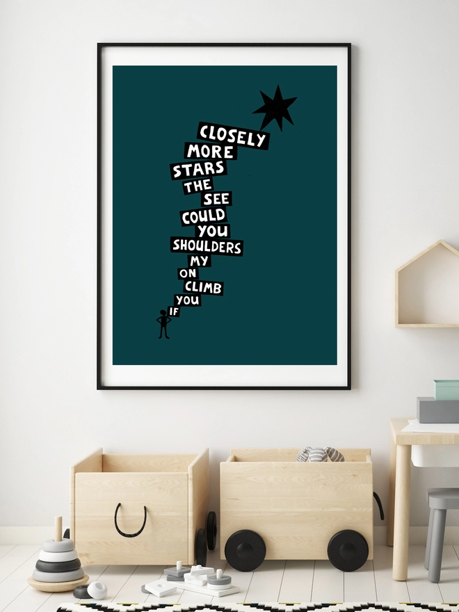 A print is framed in a black frame hanging on a child's bedroom wall. The print is dark, inky green and features the silhouette of a boy with typographic words going up to a star. The words say: 'If You Climb On My Shoulders You Could See The Stars More Closely.'   