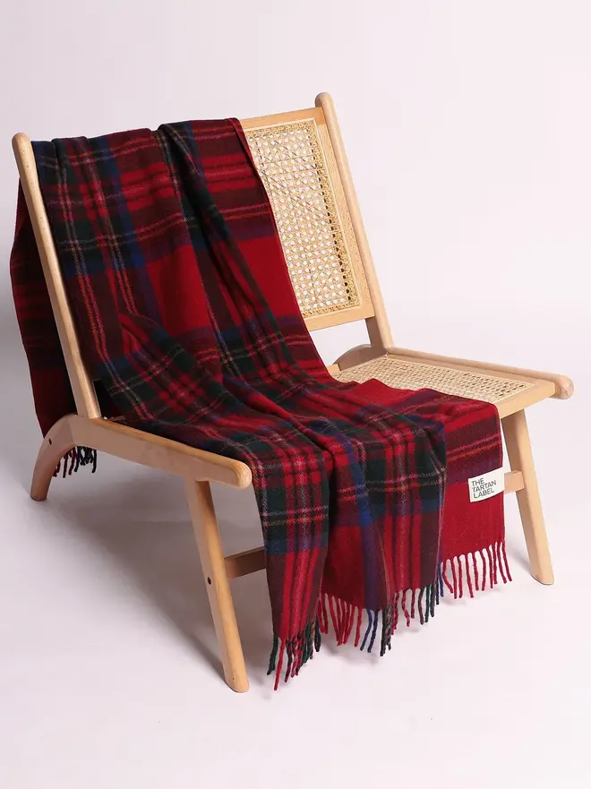 Royal Stewart Blanket, a red blanket draped over a wooden chair on a white surface against a plain backdrop. 