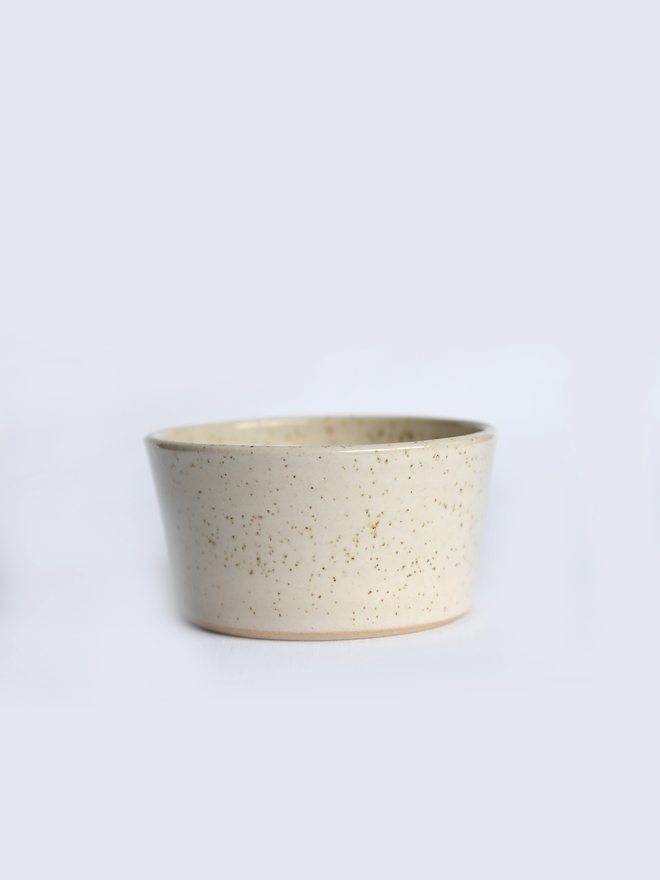 A small handmade ceramic side bowl in glossy pepper white glaze, with a tapered sides and a wide open rim, photographed against a plain light grey background