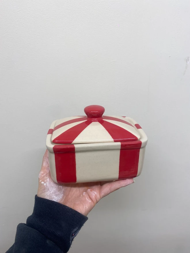 Circus Tent Stripes Handmade Ceramic Butter Dish, a red patterned butter dish held against a white backdrop. 