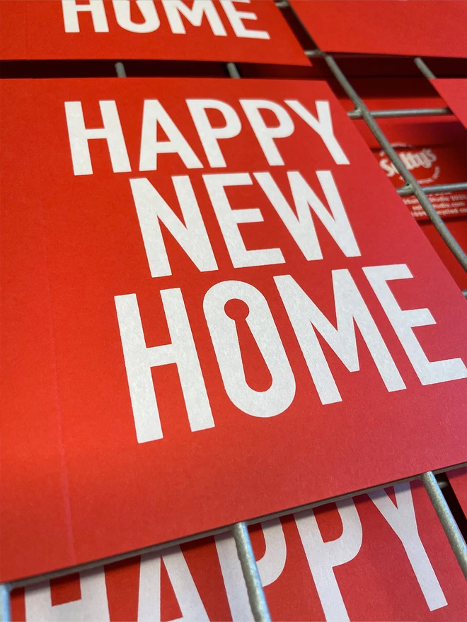 Close up of a bright red portrait card with Happy New Home printed in white ink. A keyhole shape forms the negative space inside the letter O in the word home 