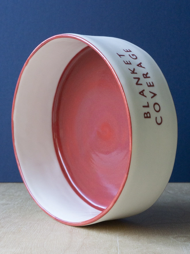 Ceramic porcelain dish with Blanket Coverage written on the side. A white Christmas serving dish with red rim and interior.