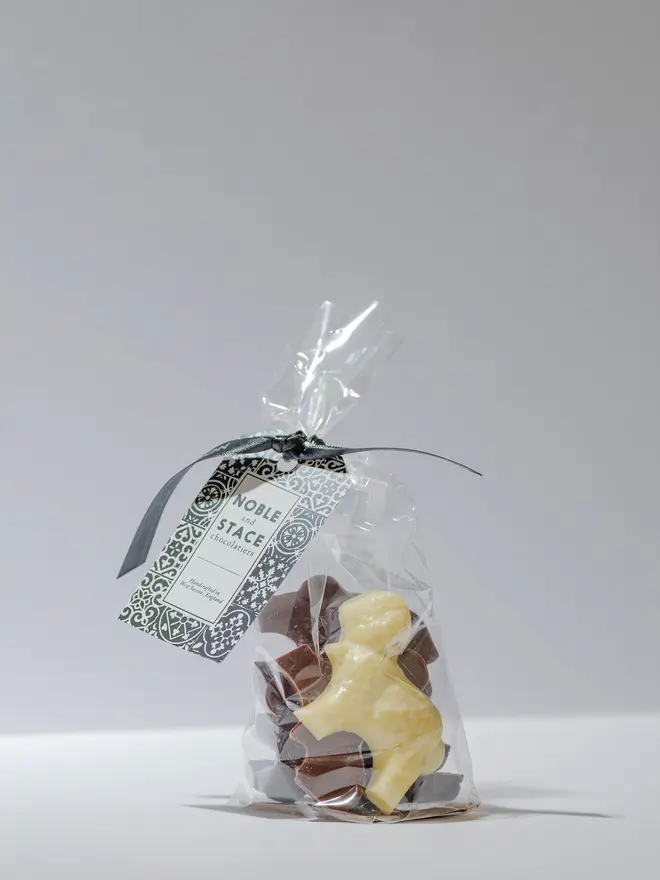 Three small solid chocolate Easter lambs in white and milk chocolate, wrapped in clear plastic on a plain white background.