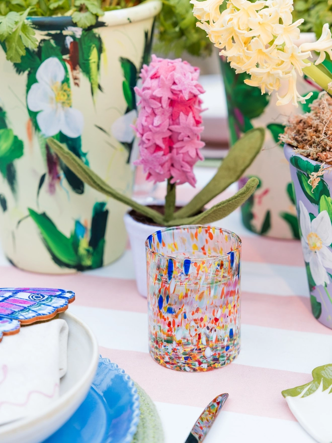 straight Murano style glass in rainbow speckles colour, on a spring tastemaker table surrounded by other colourful products such as cutlery and a striped tablecloth