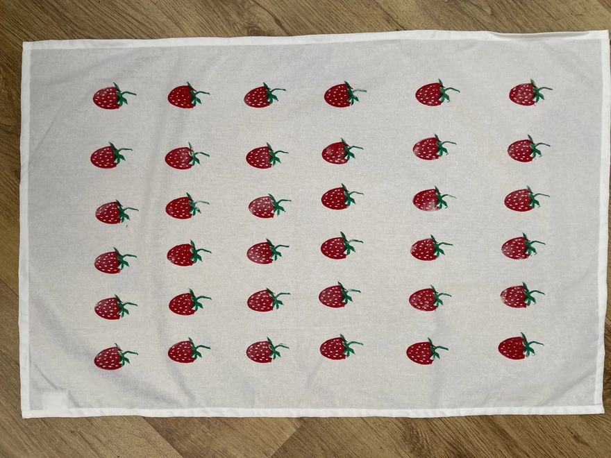 Cotton kitchen tea towel with strawberry pattern laid on a wooden table.