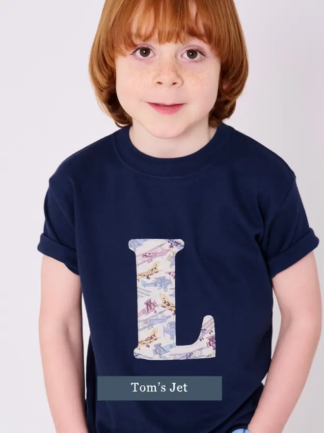 a 5 year old boy wearing a personalised navy t-shirt with his initial cut from liberty print featuring jet planes