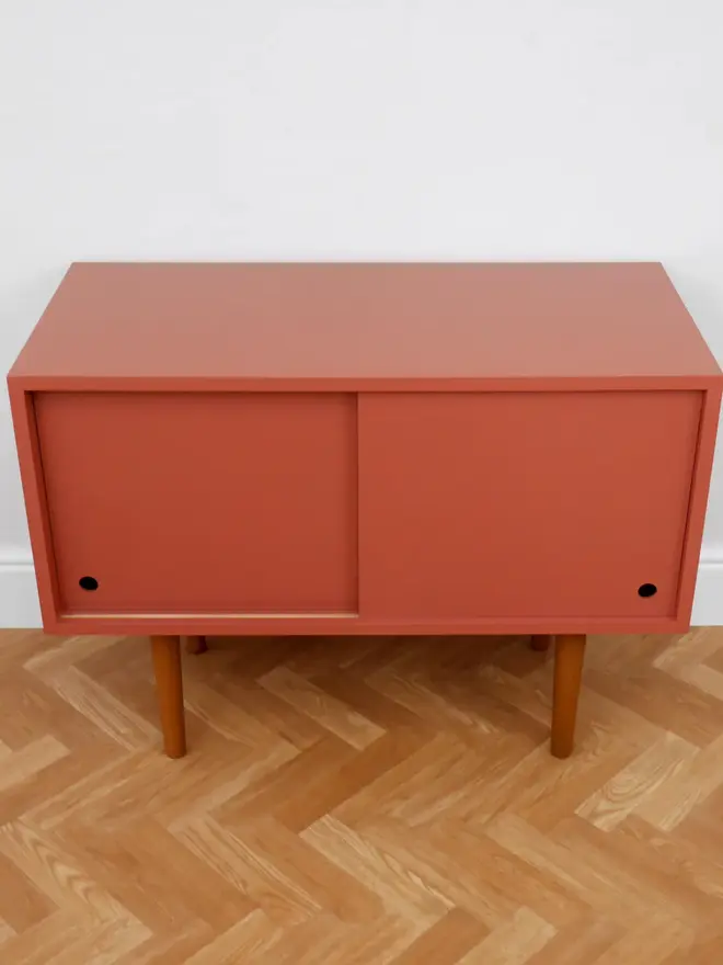 Mid-century cabinet with coral sliding doors and wooden tapered legs.