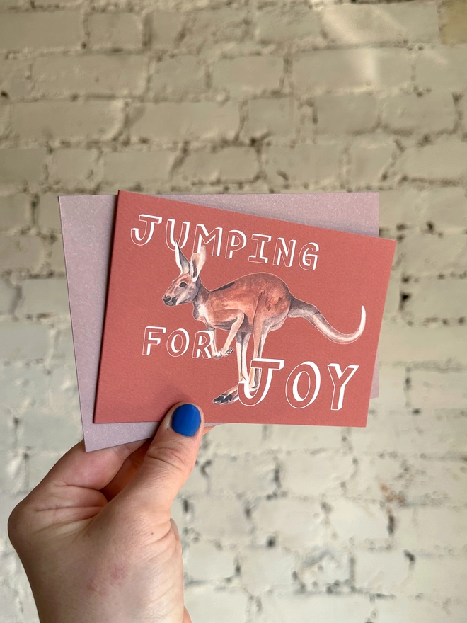 a rusty red greetings card featuring an illustration of a kangaroo with the text “jumping for joy”