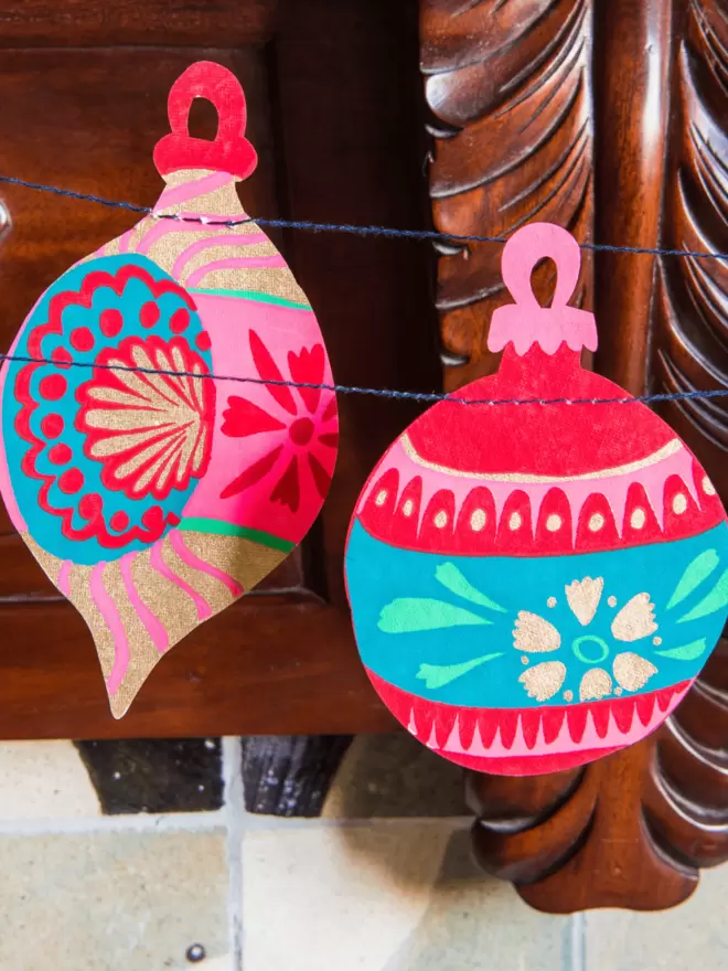 2 of the pink bauble decorations up close with blue and green details on each design