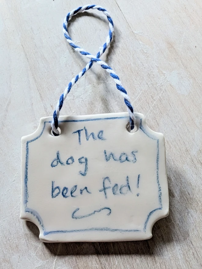 the dog has been fed sign in blue and white ceramic hanging decoration