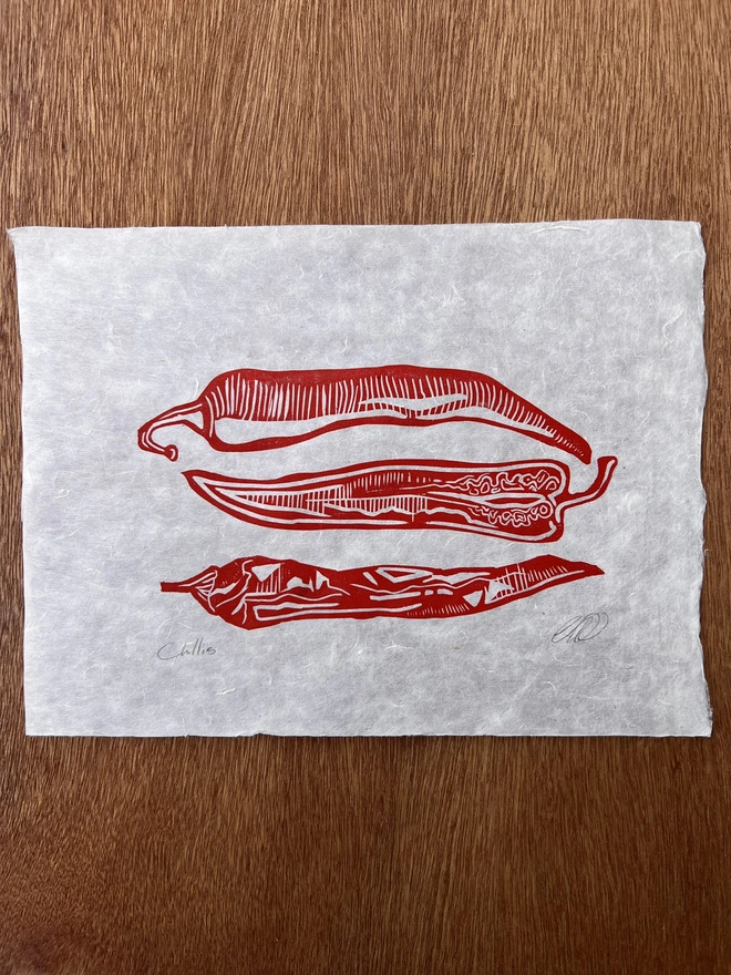 Hand printed chilli lino print featuring vibrant chillies with detailed botanical shapes and a bold folk-inspired design, printed on natural paper.
