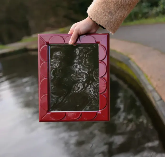 Scallop wood mirror with a scalloped wooden frame being held above a lake.