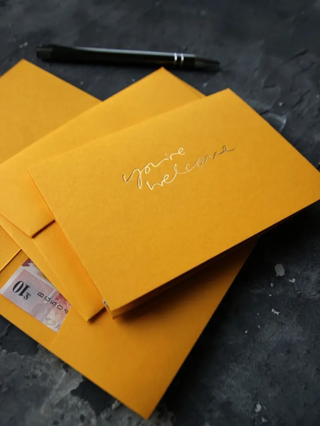 Hand foiled cash card or money wallet in a citrine colour in shiny gold foil text which says ‘you’re welcome’.