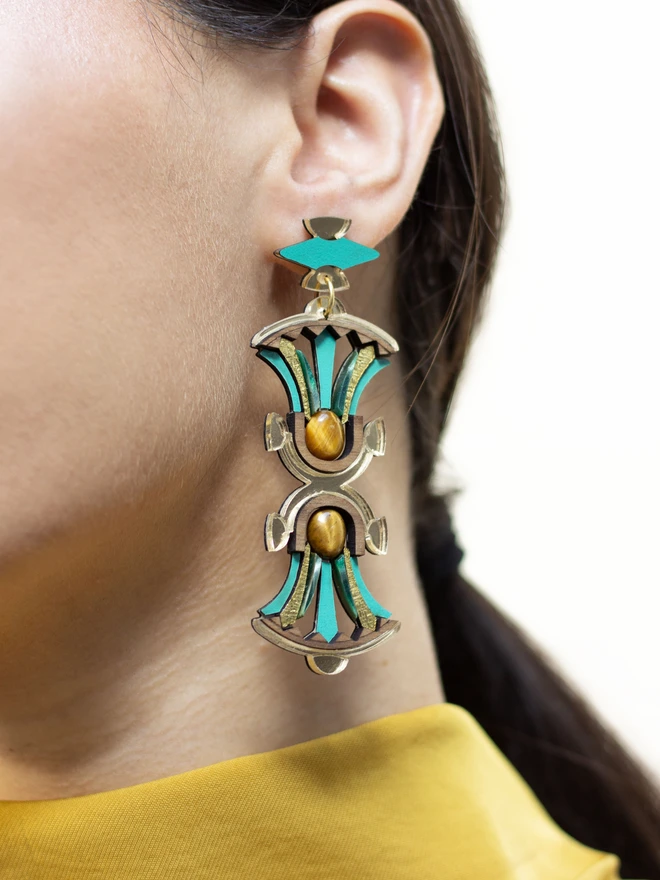 Close-up of a person wearing a gold and green earring with a blurred background
