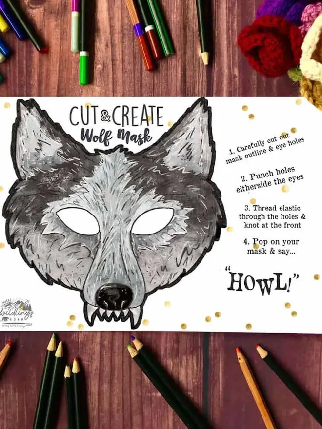 Cut And Create Forest Animals Children’s Masks Kit, an illustrated grey wolf face, surrounded by coloured pencils on a dark wood background.