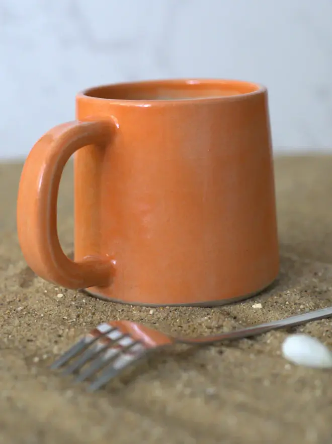 orange ceramic mug on a sandy surface