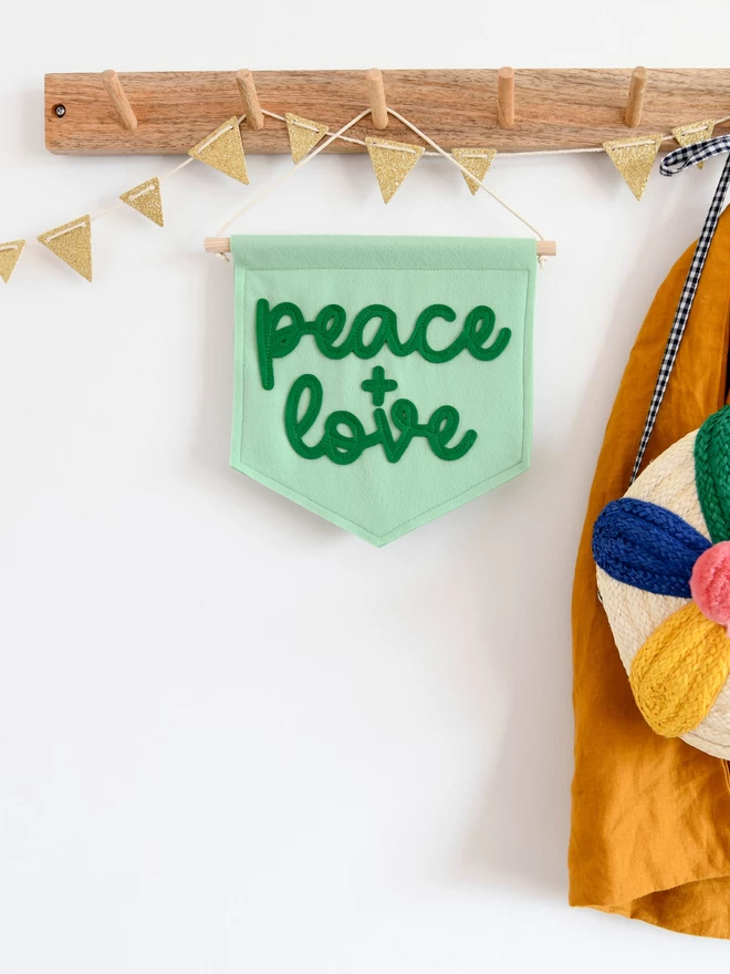 felt wall banner with the words peace and love sewn on in cursive font.