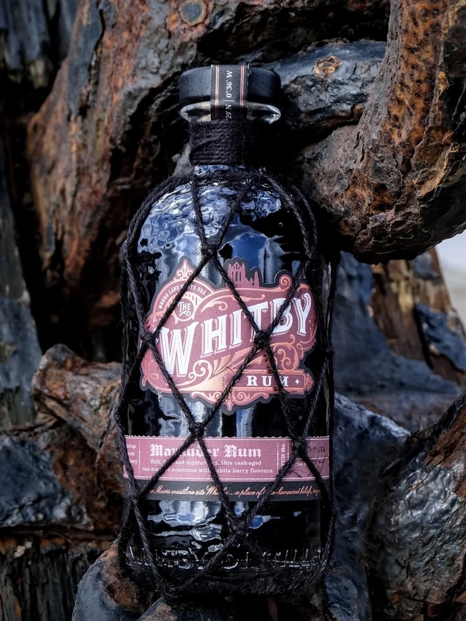 Whitby Marauder Rum: Gothic Dark Cherry Rum Edition, a bottle of rum sitting in the wood outdoors. 