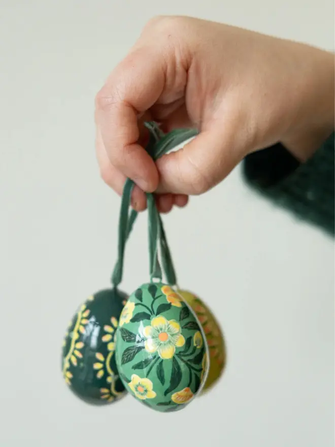 Group shot of hand painted decorative eggs on velvet string held up by a hand
