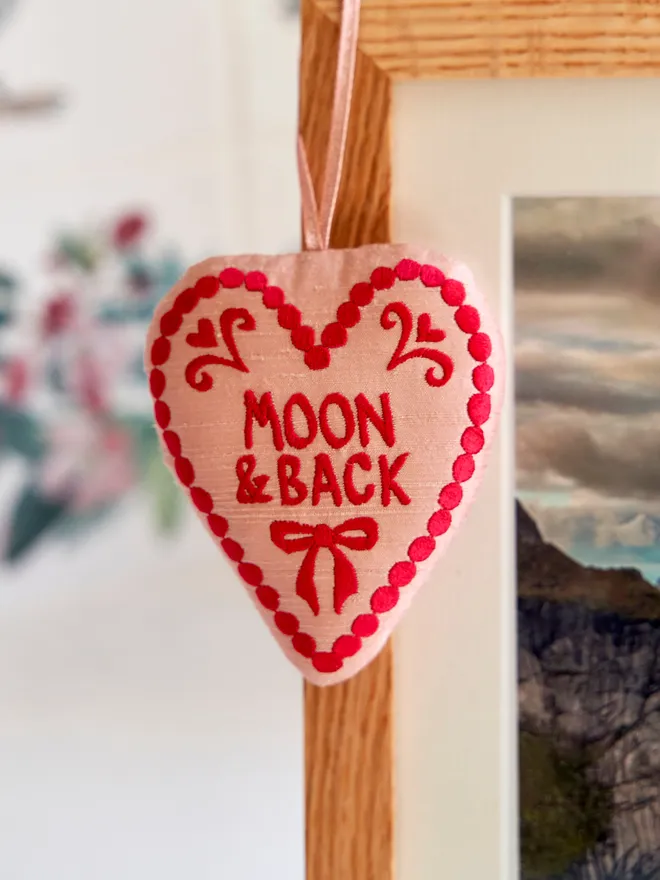 Silk Heart hanging decoration hanging on the corner of a wooden photo frame with the words 'to the moon and back'