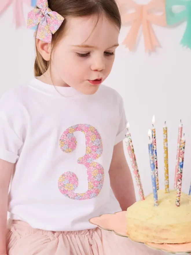a 3 year old girl wearing a white birthday t-shirt with a number 3 cut from liberty floral print on the front