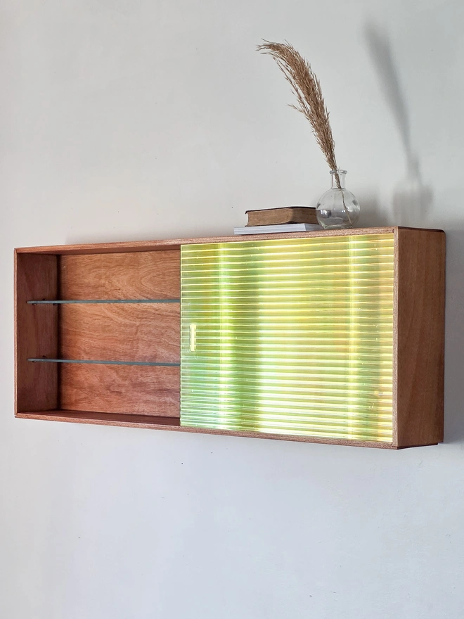 Shows a shimmering iridescent reeded glass sliding door to one side of a mid century wall cabinet