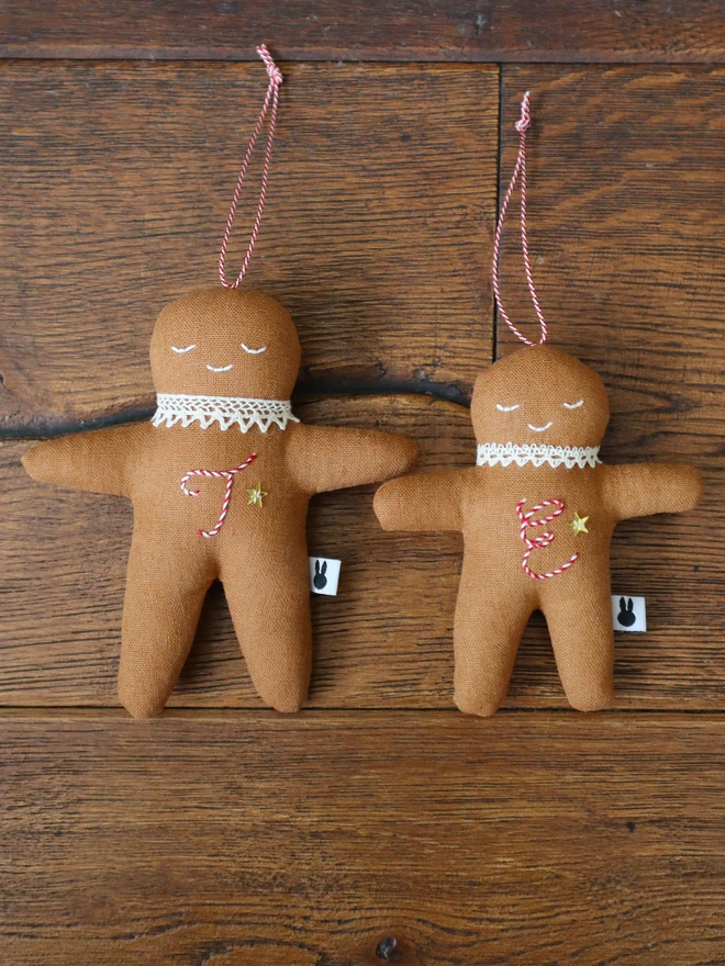 Brown linen gingerbread man christmas tree ornament with a letter hand embroidered in candy cane colours, star shaped sequin, crochet cotton lace around the neck, smile embroidered in white and candy cane colour string to hang. 