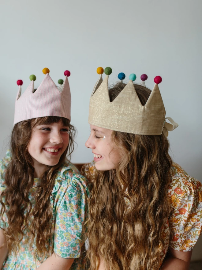 Two girls wearing their pom pom crowns smiling at each other