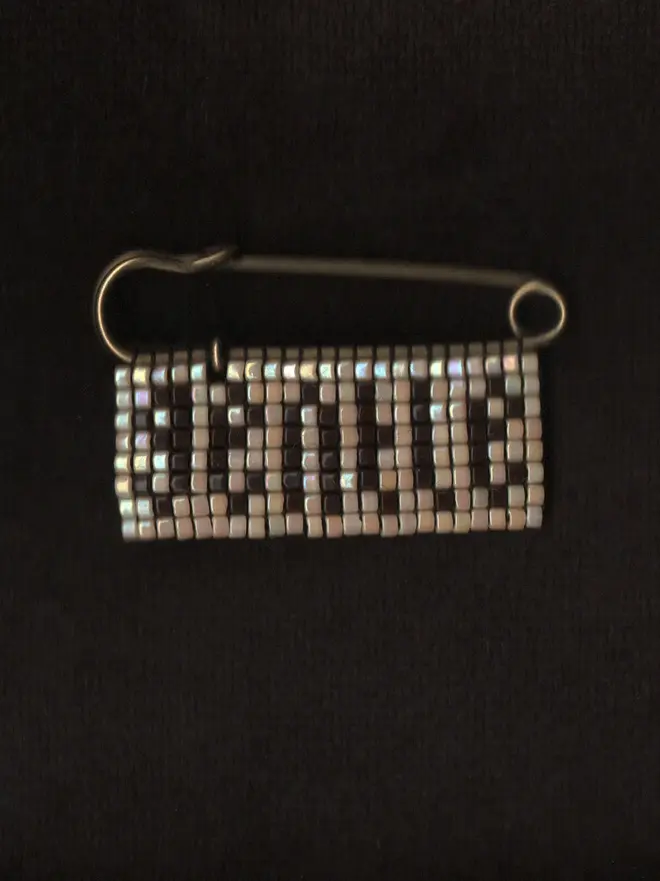 'lingua iv' beaded 'gentle' pin. a pin badge with the word gentle in brown lettering on a pearl background.