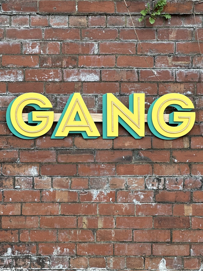 A Wooden sign reading GANG hangs on a red brick wall 