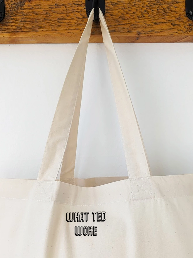 A hanging natural coloured canvas tote with a black What Ted Wore logo