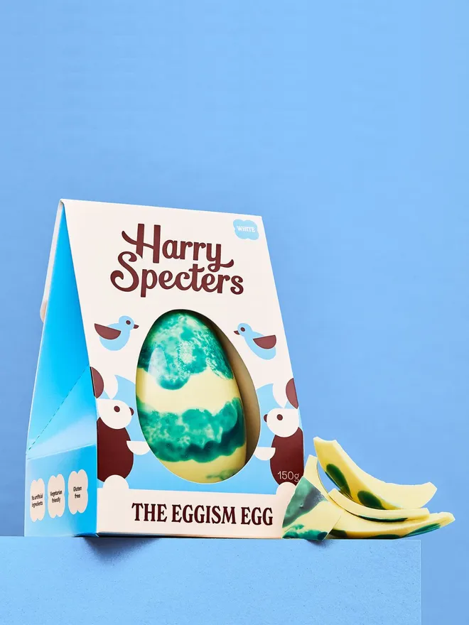 A white chocolate Easter egg decorated with blue cocoa butter, next to a stack of white chocolate Easter egg pieces