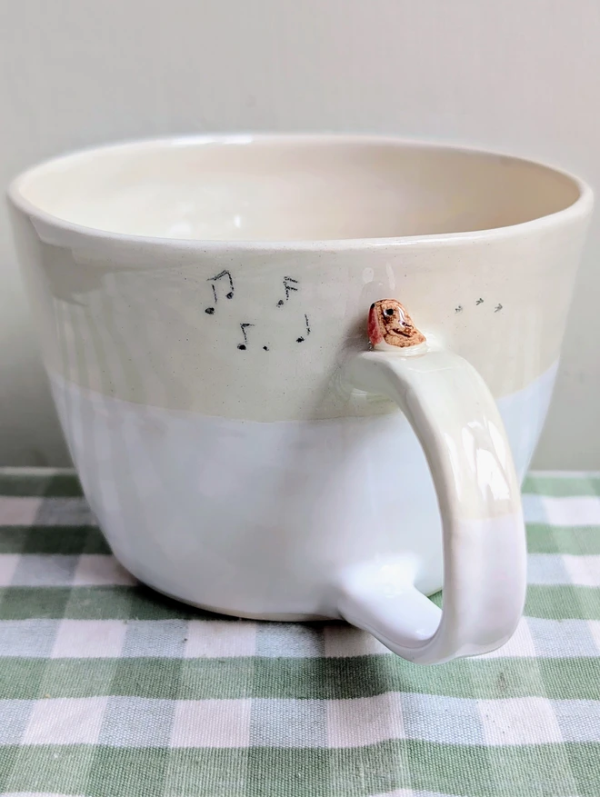 white ceramic cup with a tiny robin bird on the handle with bird prints and musical notes on the mug