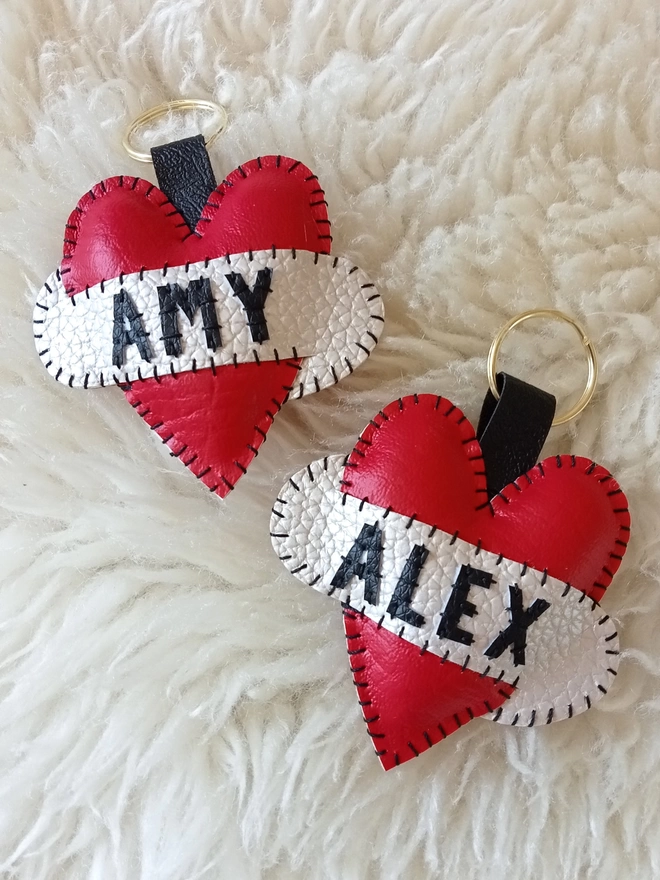 Two red leatherette tattoo style keyrings, with black lettering across white scrolls. One says AMY, the other, ALEX