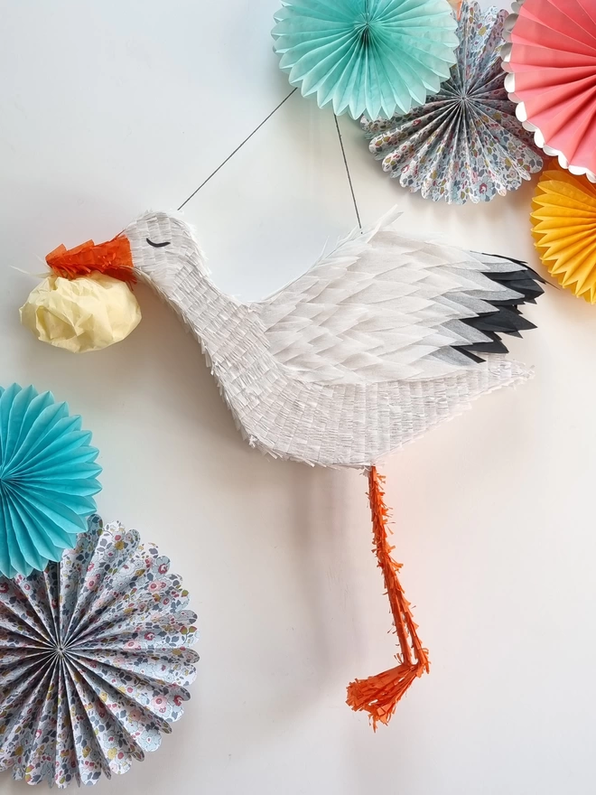 Stalk Pinata by pinyatay carrying a baby bundle on white surrounded by pastel paper decorations