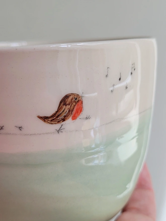 close up of a green ceramic tumbler with a small robin painted on the side with bird prints and musical notes