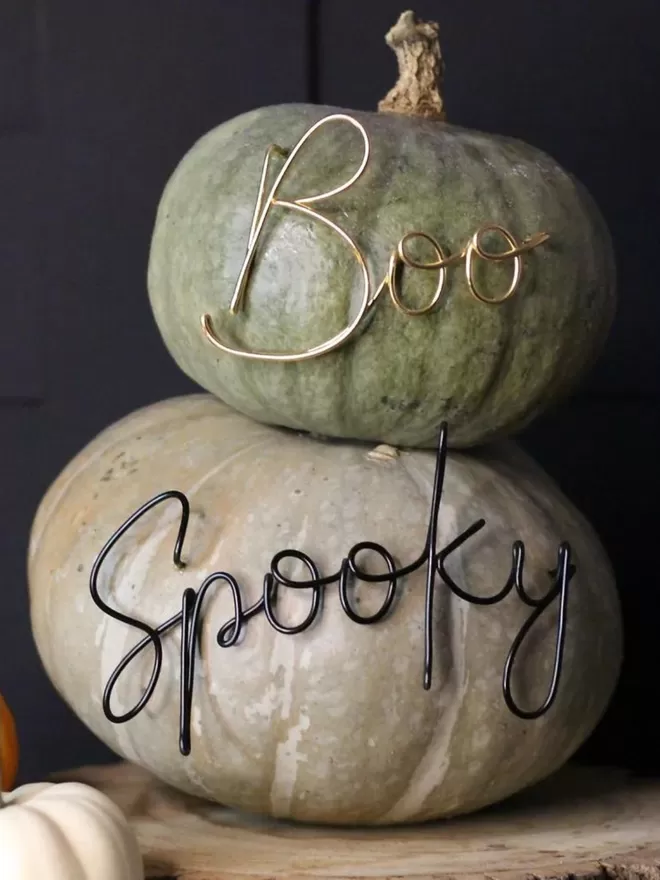 Black spooky sign seen in a pumpkin with a gol boo above in a green pumpkin ready for halloween.