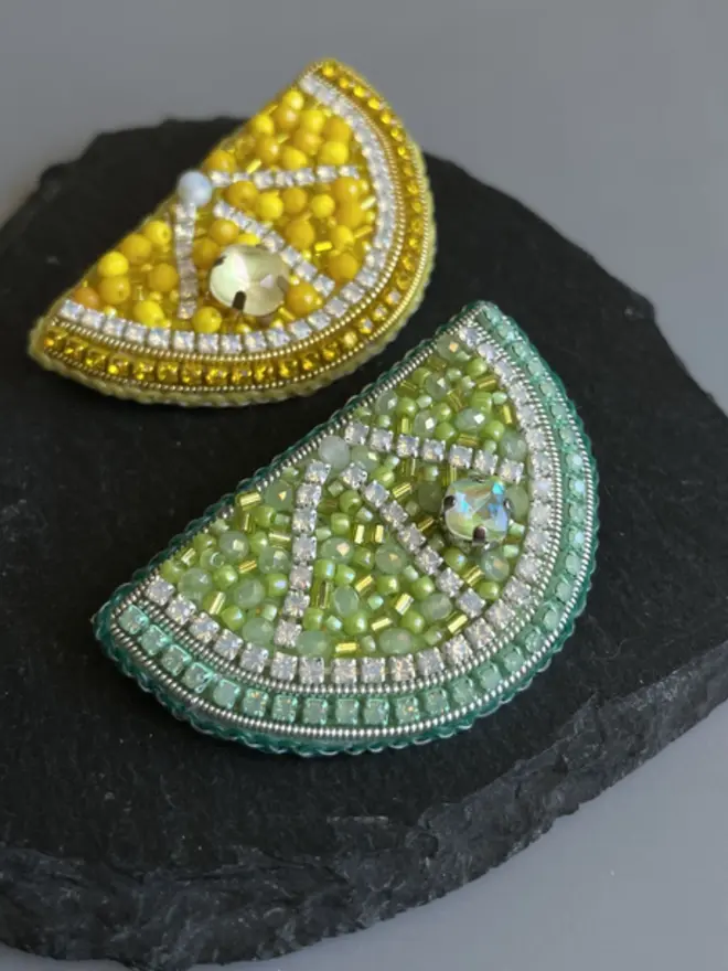 Lemon and lime slice beaded brooch, placed on  a black slate in the shape of a heart. 