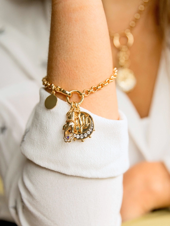 Women wearing a gold belcher chain bracelet with gold lotus moon charm and gold hand charm