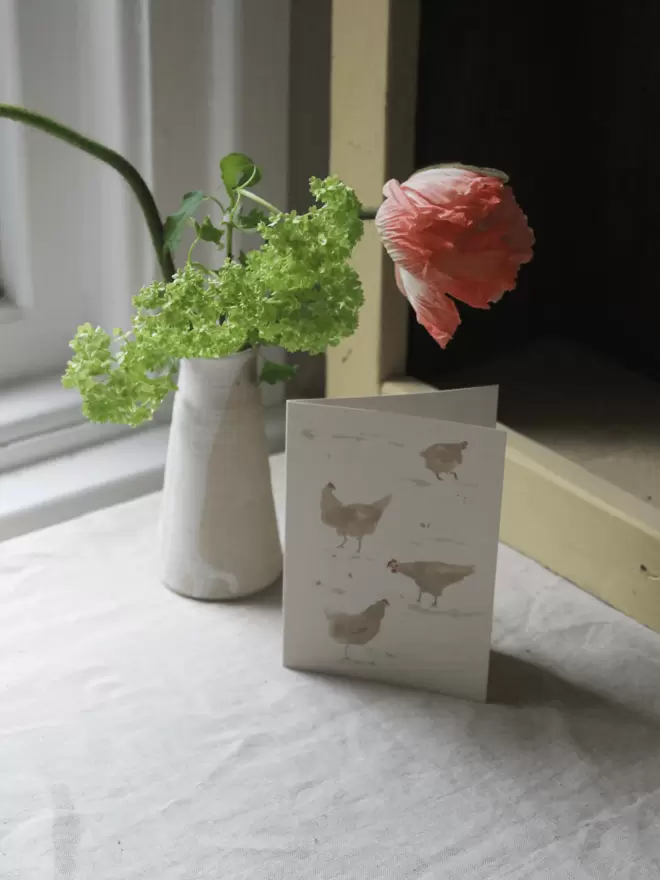 chickens card next to vase of poppies.