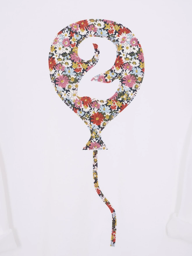 A white cotton long sleeve t-shirt. The t-shirt features a balloon with the number 2 cut out from it, appliquéd in a floral Liberty print. A close up of the stitching.