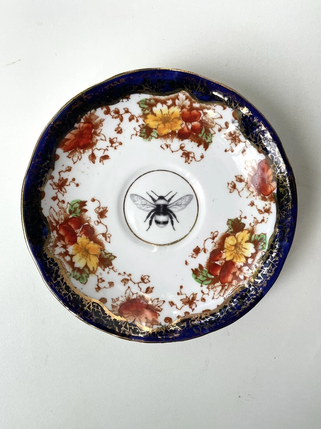 vintage plate with navy edge and orange floral border and in the centre is an illustration of a bee
