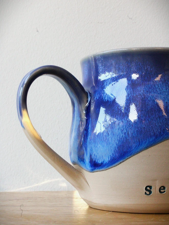Close up of Blue and natural ceramic mug with 'Sea Please' stamped