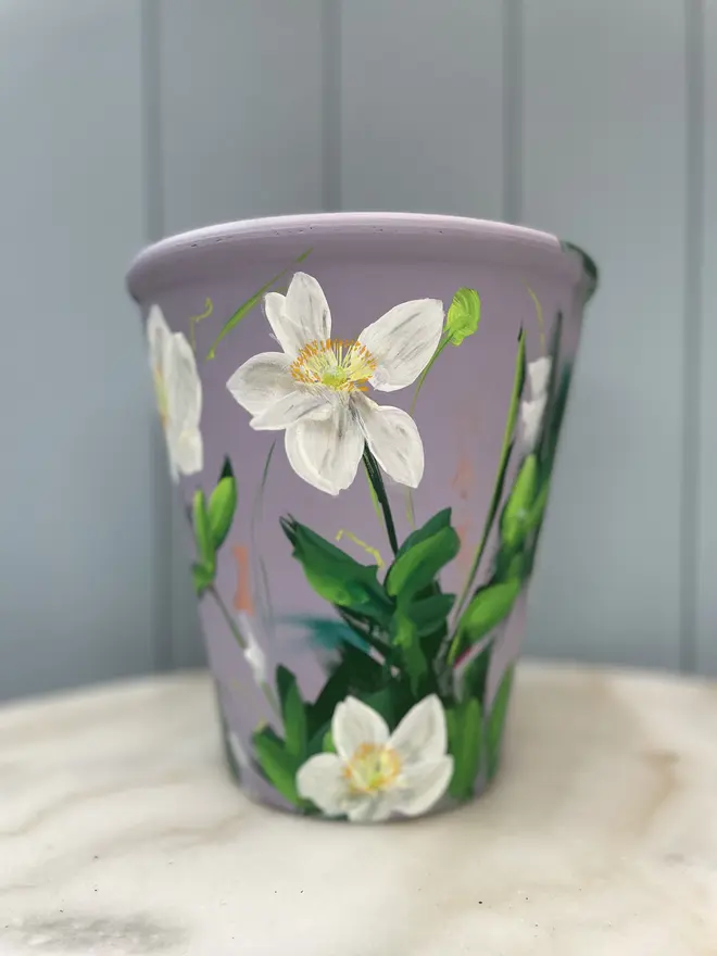 Unique hand-painted terracotta pot featuring white anemone flowers on a lilic background