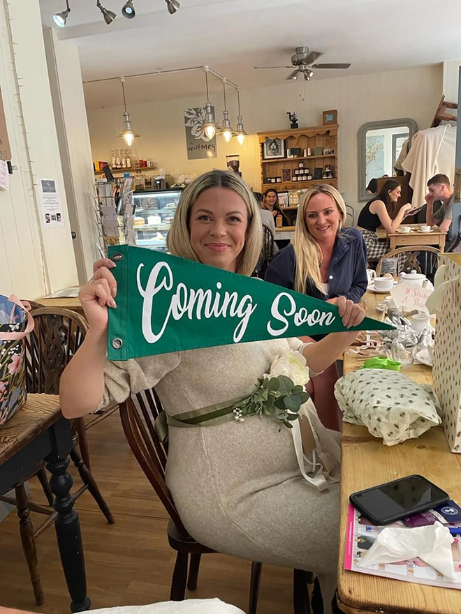 A Green pennant flag with the words 'Coming Soon' he'd by a lady at a baby shower.
