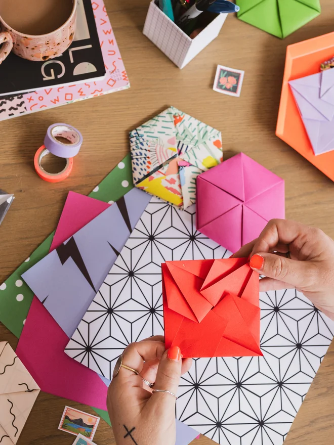 Woman holding origami envelope with papers and other envelopes on a table below.